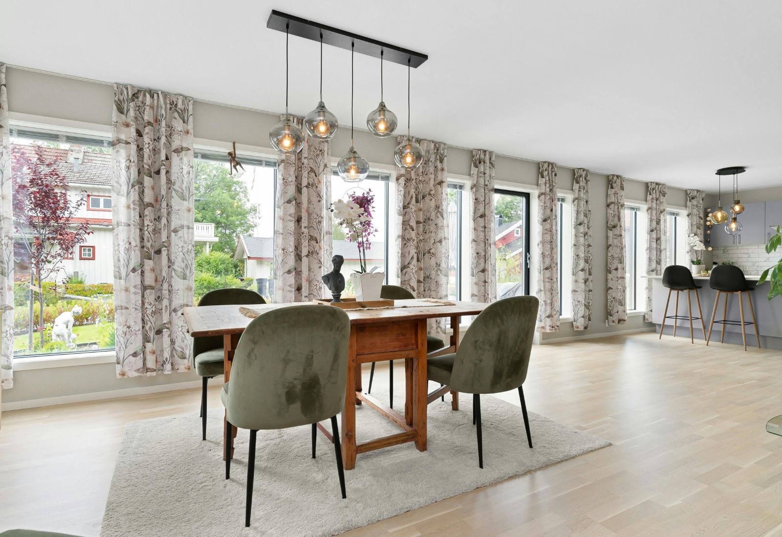 Suspension multiple à globes en verre au-dessus d’une table en bois dans une salle à manger ouverte sur la cuisine.